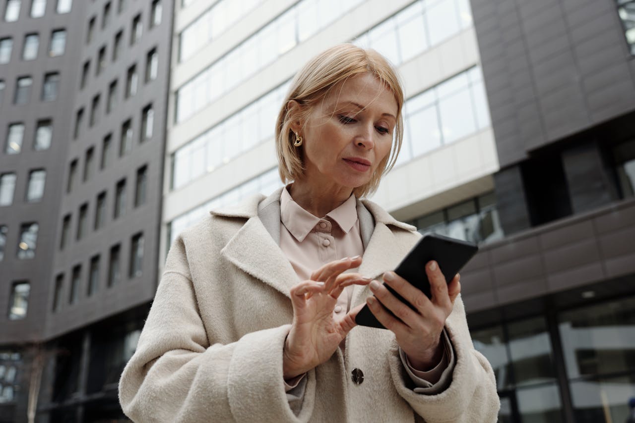 why-choose-us Woman in coat using smartphone in front of modern building. Professional and focused expression.